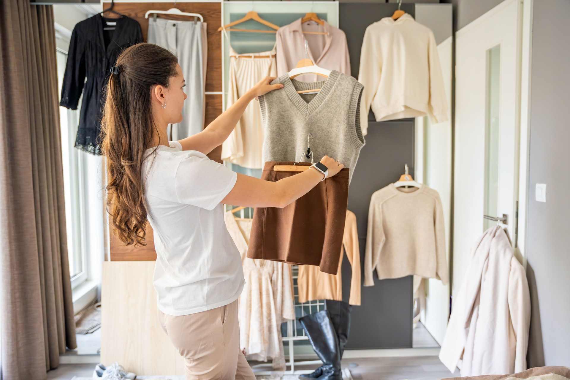 Young woman stylist in front of wardrobe filled with diverse clothing, analyzing outfit combinations. Creating fashionable looks requires attention to detail, color coordination, keen sense of style